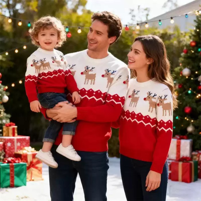 family-matching-red-reindeer-christmas-sweaters ather holding toddler while posing with mother outdoors in matching red and white reindeer Christmas sweaters.