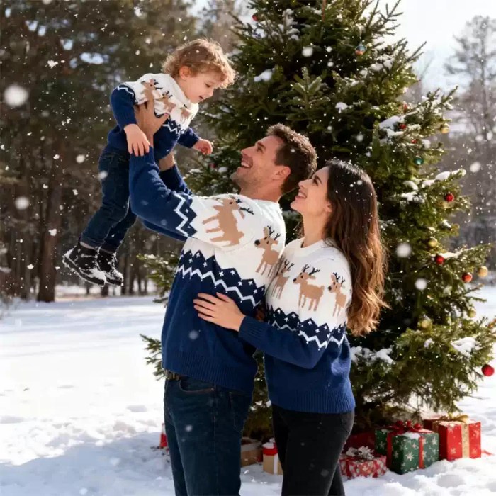 family-navy-reindeer-sweaters-snow-outdoors Father lifting toddler in snowy outdoor setting while family wears matching navy blue reindeer holiday sweaters.