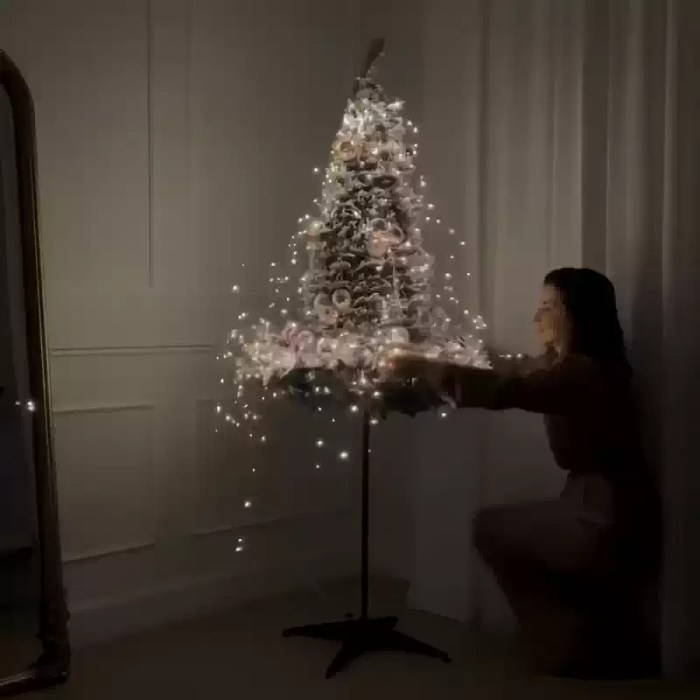 Foldable flocked Christmas tree being opened with built-in lights.