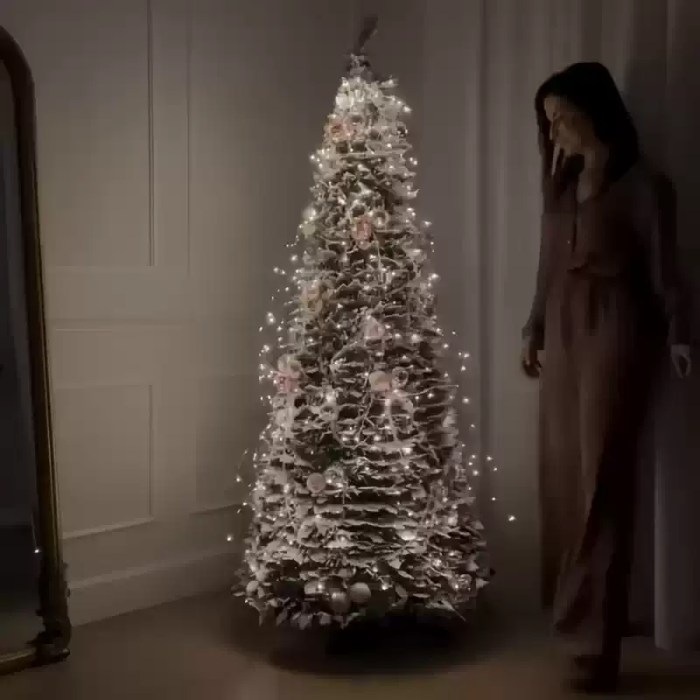 Pre-lit flocked Christmas tree with warm white lights indoors.